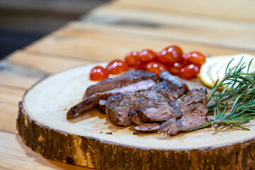 Steak Slice on the wood plate, Decoration by Lemon slice, tomato, and rosemary on the wood table in low light ambience.