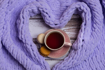 Cup of tea with macaroons with a heart-shaped plaid around. Concept of cozy holidays.