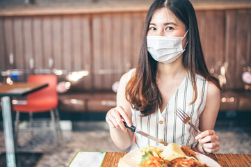 Asian woman sitting separated in restaurant eating food .keep social distance for protect infection from coronavirus covid-19, restaurant and social distancing concept.