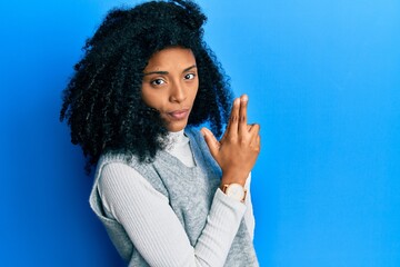 African american woman with afro hair wearing casual winter sweater holding symbolic gun with hand gesture, playing killing shooting weapons, angry face