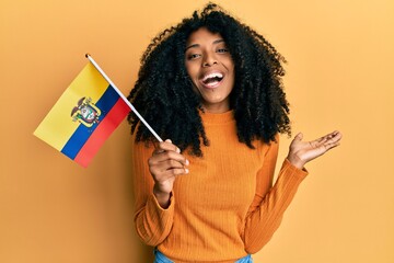 African american woman with afro hair holding ecuador flag celebrating achievement with happy smile and winner expression with raised hand - obrazy, fototapety, plakaty