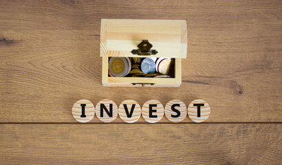 Invest symbol. Concept word invest on wooden cubes on a beautiful wooden background, small wooden chest with coins. Business and invest concept.