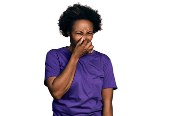 African american woman with afro hair wearing casual purple t shirt smelling something stinky and...