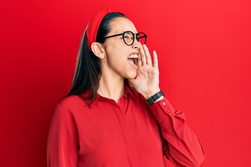 Young hispanic woman wearing casual clothes and glasses shouting and screaming loud to side with hand on mouth. communication concept.