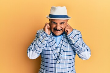 Mature middle east man with mustache wearing vintage and elegant fashion style covering ears with fingers with annoyed expression for the noise of loud music. deaf concept.