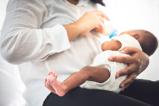 Blurred soft images of mother Sitting on bed, and feed milk from bottle milk to her 12-day-old African baby black skin newborn son, This picture focused on foot baby, to food for infant concept.