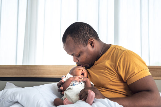 African father Blow air on his 12-day-old black skin baby newborn son's forehead to convince him to sleep, on white bed in bedroom, to relationship African family and baby black skin concept.