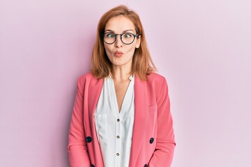 Young caucasian woman wearing business style and glasses making fish face with lips, crazy and comical gesture. funny expression.