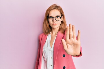Young caucasian woman wearing business style and glasses doing stop sing with palm of the hand. warning expression with negative and serious gesture on the face.