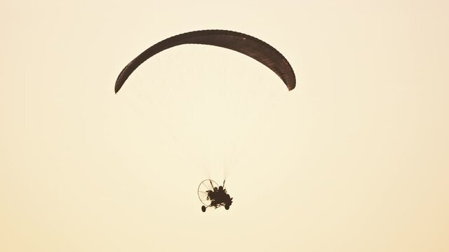 Evening paramotor flight. Parachute against sunset sky. Tandem motor powered paragliding at twilight. 