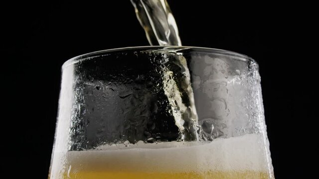 Beer pouring. Cold Beer in a glass with water drops. Fresh Beer into Glass on Black Background.