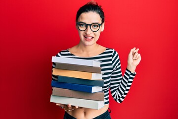 Young caucasian woman wearing glasses and holding books smiling happy pointing with hand and finger to the side