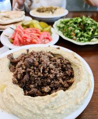 Creamy hummus with spicy mutton minced meat in clay bowl on stone background. Ramadan food.