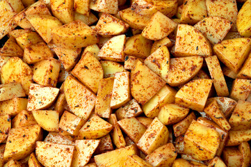 Raw potatoes sprinkled with spices. Vegetables cut into cubes prepared for baking. Place - home kitchen.