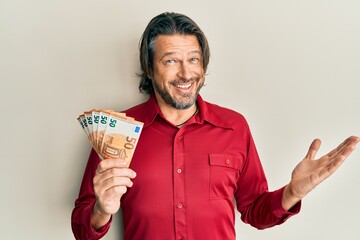 Middle age handsome man holding bunch of 50 euro banknotes celebrating achievement with happy smile...