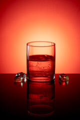A glass of whiskey with ice on a glossy table and a light background
