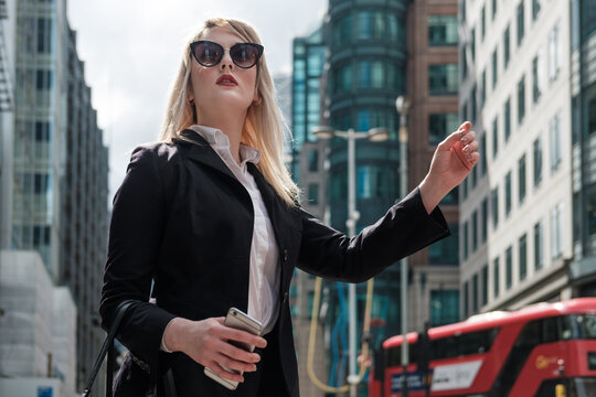 Confident Business Woman Waving A Taxi In City Of London.