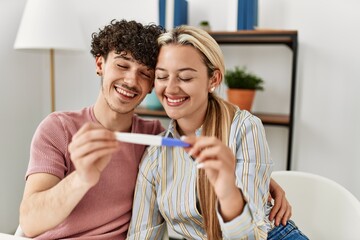 Young couple smiling happy looking pregnant test result at home.