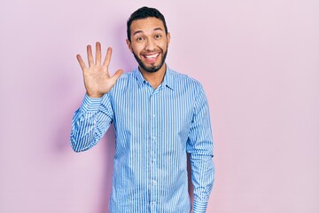 Hispanic man with beard wearing casual blue shirt showing and pointing up with fingers number five while smiling confident and happy.