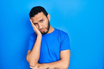 Hispanic man with beard wearing casual blue t shirt thinking looking tired and bored with depression problems with crossed arms.