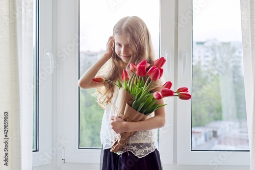 Mother's day, girl child with bouquet of red tulips flowers at home