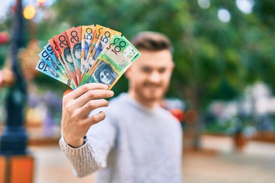 Young caucasian man smiling happy holding australian dollars at the park.