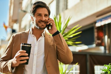 Young hispanic businessman talking on the smartphone and drinking coffee at the city.