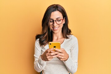 Young brunette woman using smartphone over yellow background smiling with a happy and cool smile on face. showing teeth. - Powered by Adobe