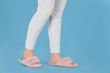 Woman in fluffy slippers on light blue background, closeup