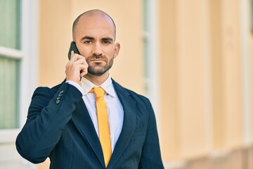 Young hispanic bald businessman with serious expression talking on the smartphone at the city.