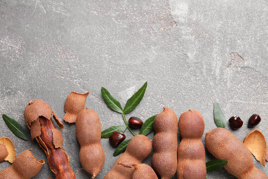 Ripe tamarinds and fresh leaves on grey table, flat lay. Space for text