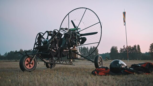 Paramotor trike, safety clothing and gear laying on airport grass. Tandem motor powered paragliding at twilight. 