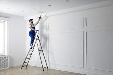 Handyman painting ceiling with white dye indoors, space for text - obrazy, fototapety, plakaty