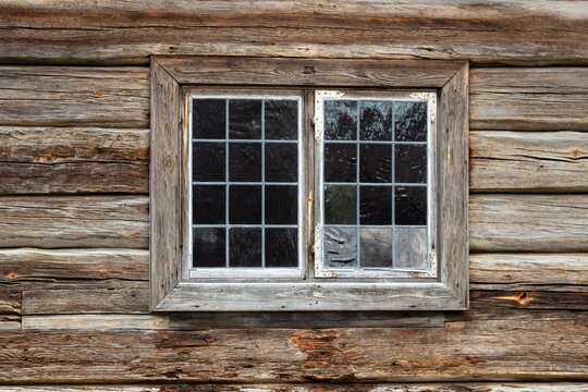 Old window with handmade glas panes on a 200 years old wooden log cottage. Natural aged wood surfaces