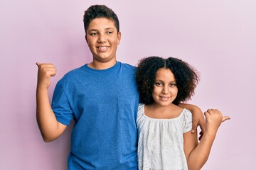 Young hispanic family of brother and sister wearing casual clothes together pointing to the back behind with hand and thumbs up, smiling confident