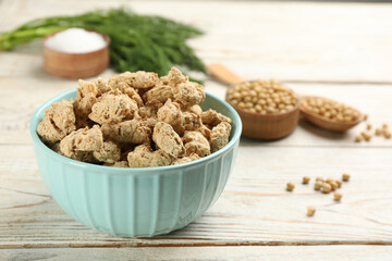 Dehydrated soy meat chunks in bowl on white wooden table. Space for text