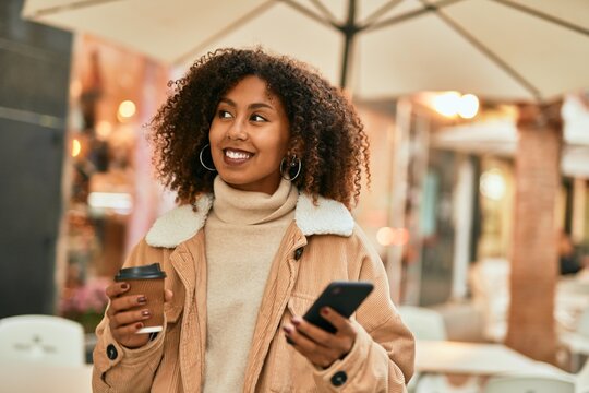 Young african american woman using smartphone and drinking coffee at the city.