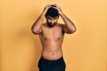 Arab man with beard wearing swimwear shirtless suffering from headache desperate and stressed because pain and migraine. hands on head.