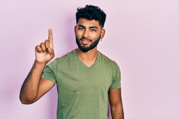 Fototapeta premium Arab man with beard wearing casual green t shirt smiling with an idea or question pointing finger up with happy face, number one