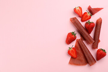 Delicious fruit leather rolls and strawberries on pink background, flat lay. Space for text