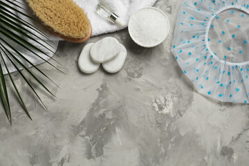 Flat lay composition with shower cap and toiletries on grey stone background. Space for text