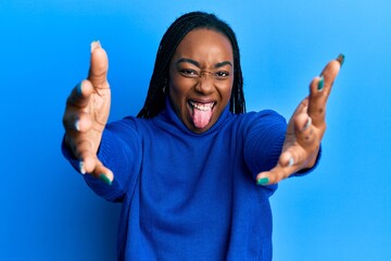 Young african american woman with arms stretched hug gesture sticking tongue out happy with funny...