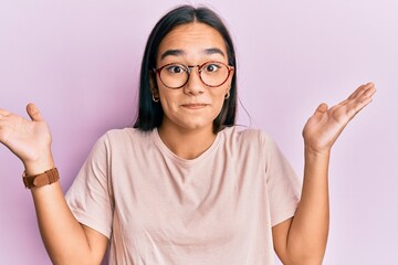 Young asian woman wearing casual clothes and glasses clueless and confused with open arms, no idea...