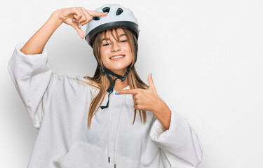 Teenager caucasian girl wearing bike helmet smiling making frame with hands and fingers with happy face. creativity and photography concept.