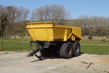 Yellow, empty trailer with big wheels on a parking lot in nature. Spring, April, Netherlands.