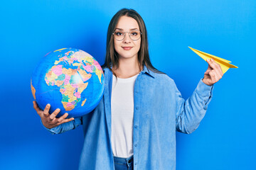 Fototapeta premium Young hispanic girl holding paper plane and world ball smiling with a happy and cool smile on face. showing teeth.