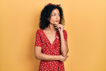 Young latin girl wearing summer dress with hand on chin thinking about question, pensive expression. smiling and thoughtful face. doubt concept.