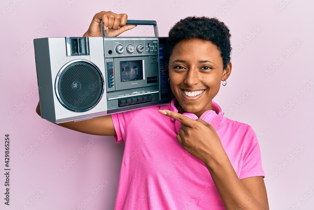 Wall mural Young african american girl holding boombox, listening to music smiling happy pointing with hand and finger