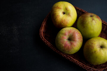 Some yellow with red apples in a basket on a black wooden table  