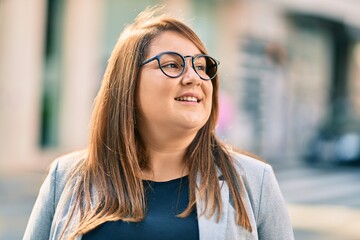 Young hispanic plus size businesswoman smiling happy standing at the city.